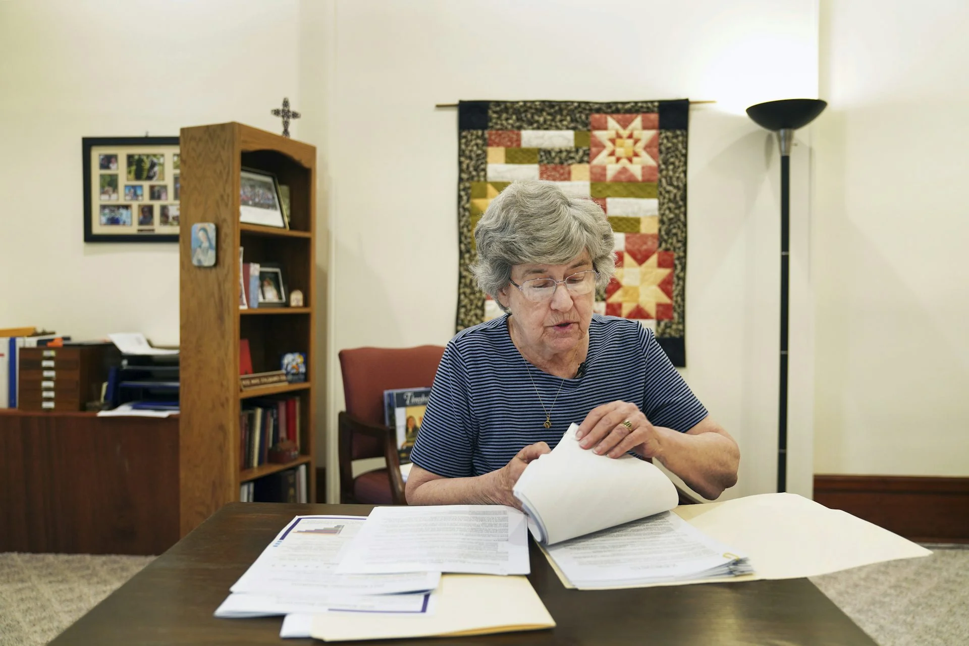 An older woman reviews a stack of papers in a big office.