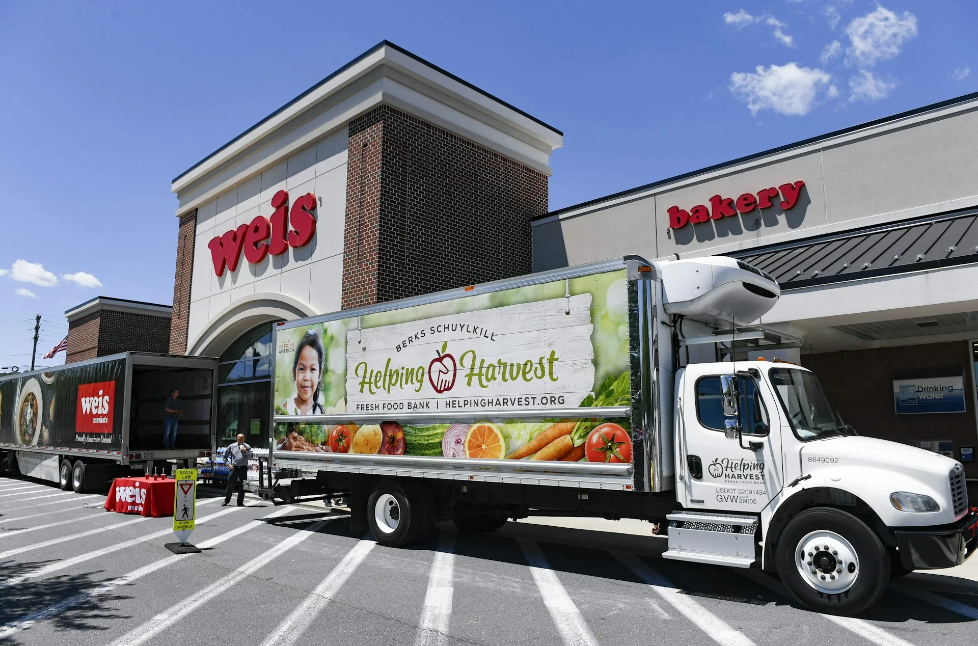 A Weis truck and a Helping Harvest Truck are parked in front of a Weis store.